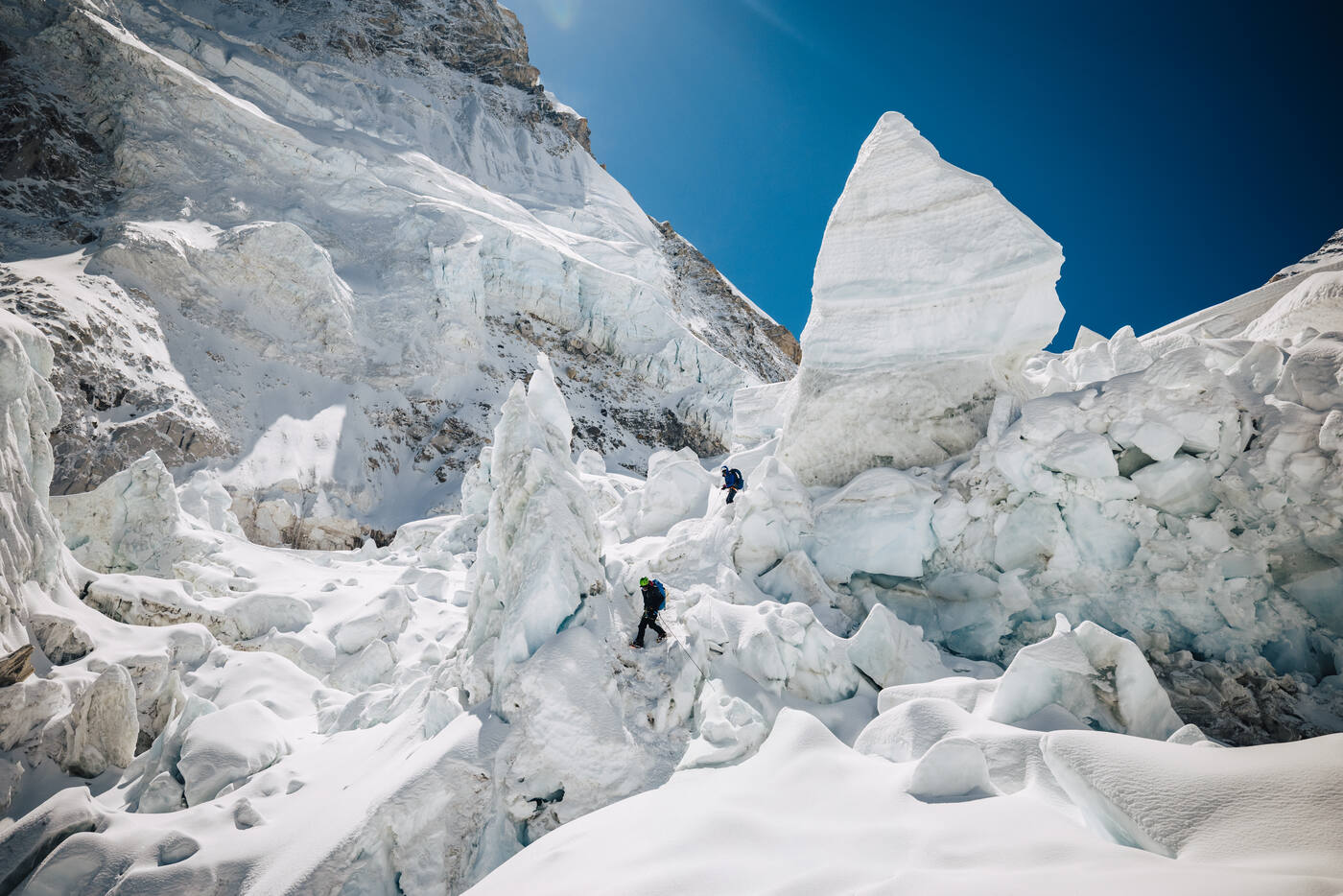 Two climbers moving between tall ice towers in the Khumbu Icefall