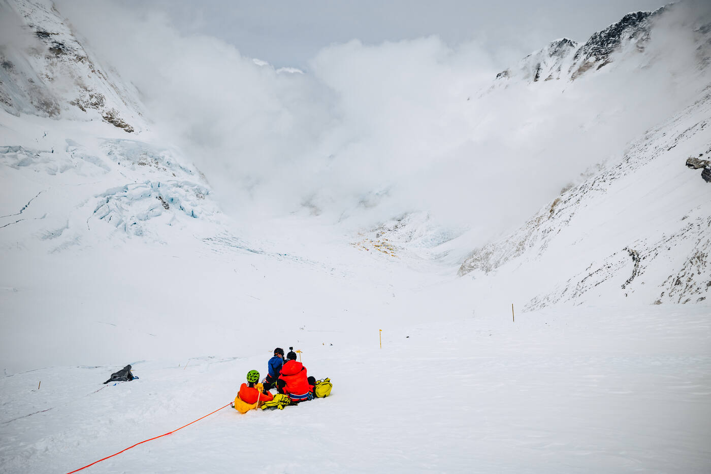 A small group of climbers resting on the snow in the upper Western Cwm below the cloud-covered Lhotse Face