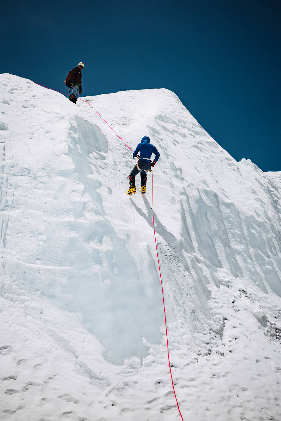 Two climbers ascending a steep ice wall on fixed rope in the Khumbu Icefall
