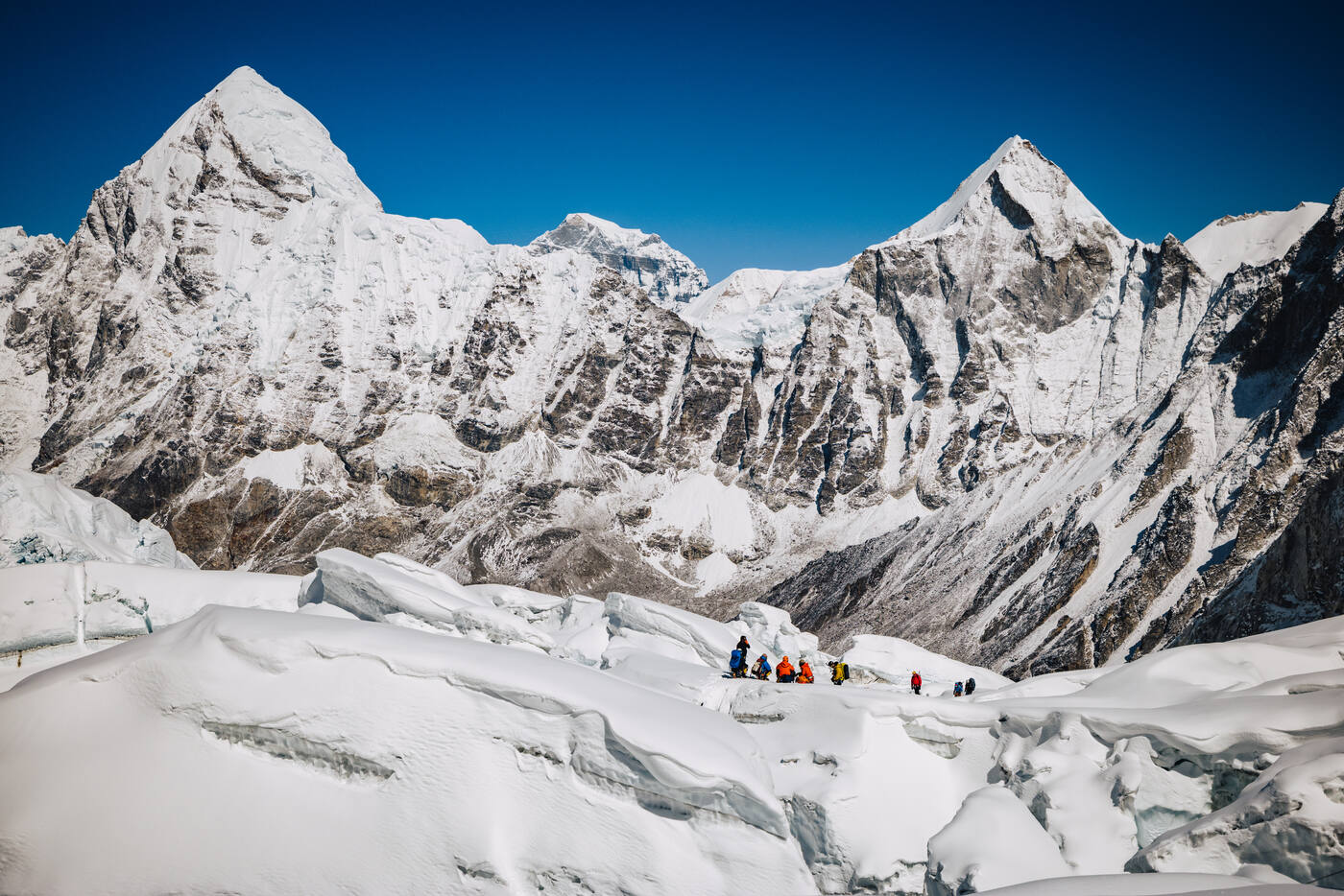 A group of climbers gathered on the snow near the top of the Khumbu Icefall with sharp snow peaks behind