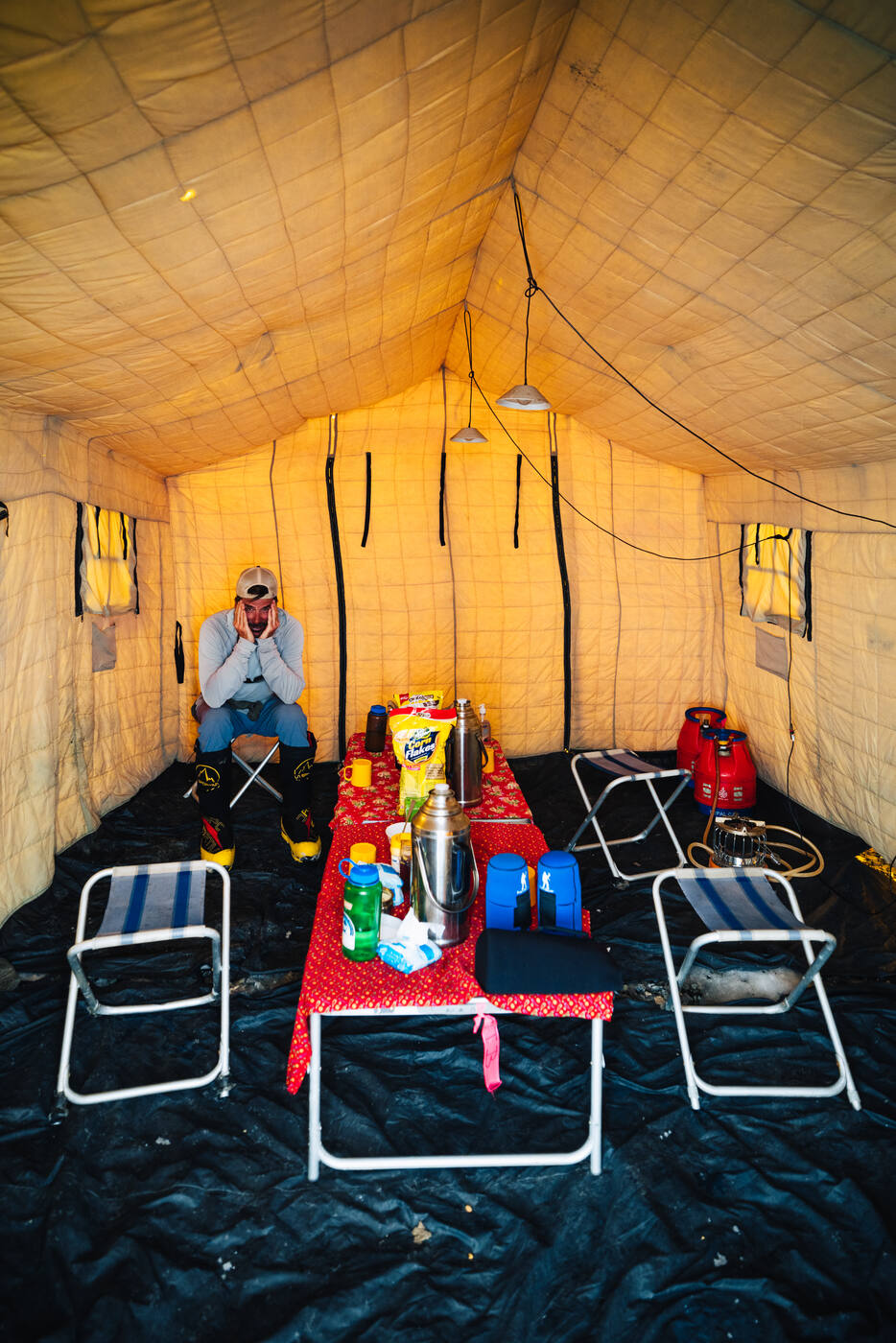 Interior of a dining tent with a red tablecloth, folding stools, and a climber seated at the end