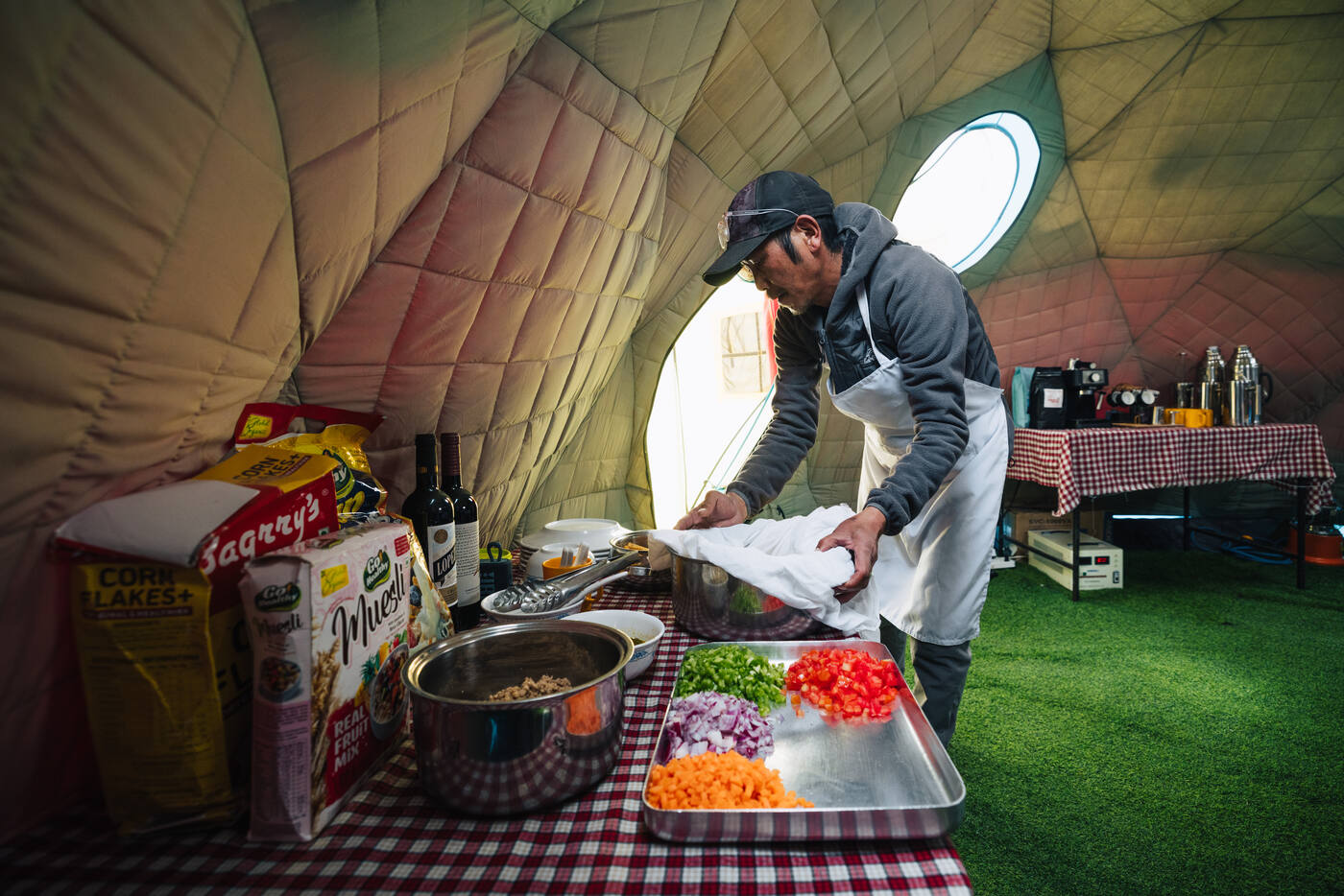 Cook preparing fresh food inside the dome tent at Everest Base Camp with chopped vegetables on a checkered tablecloth