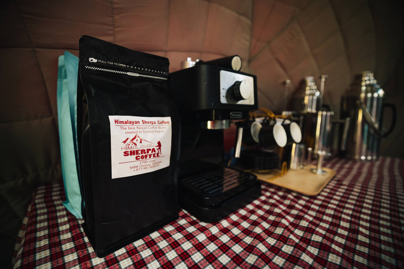 Espresso machine and a bag of Himalayan Sherpa Coffee on a checkered tablecloth inside the dining tent