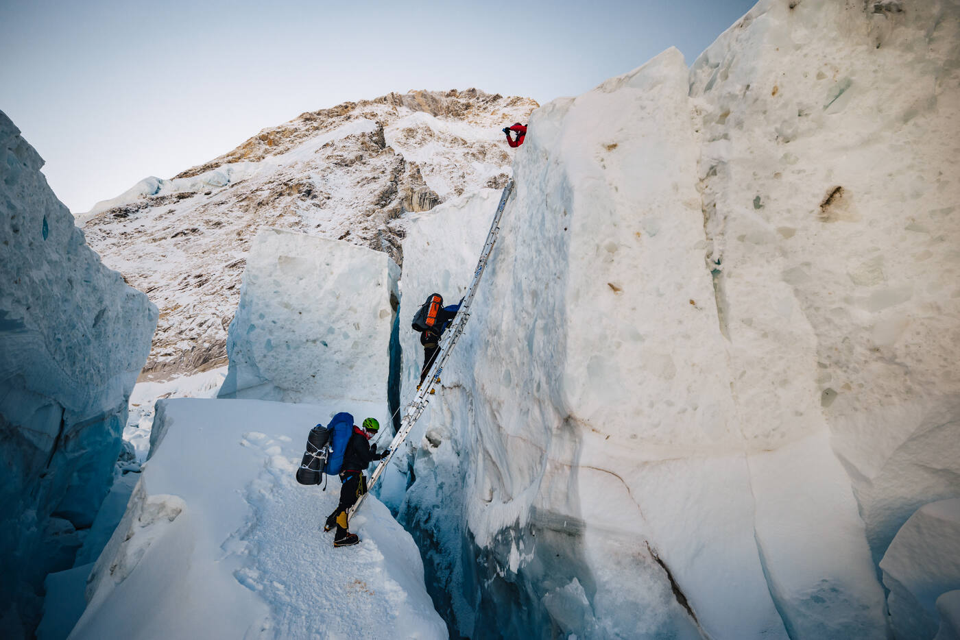 Climbers navigating through a deep ice corridor with ladders and ropes in the Khumbu Icefall