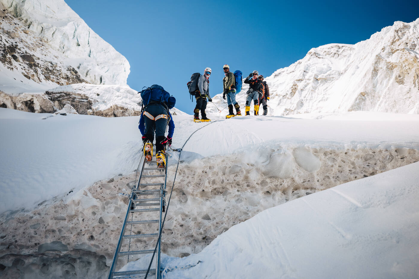 Climbers crossing a ladder bridge over a crevasse in the Khumbu Icefall with a group waiting on the other side