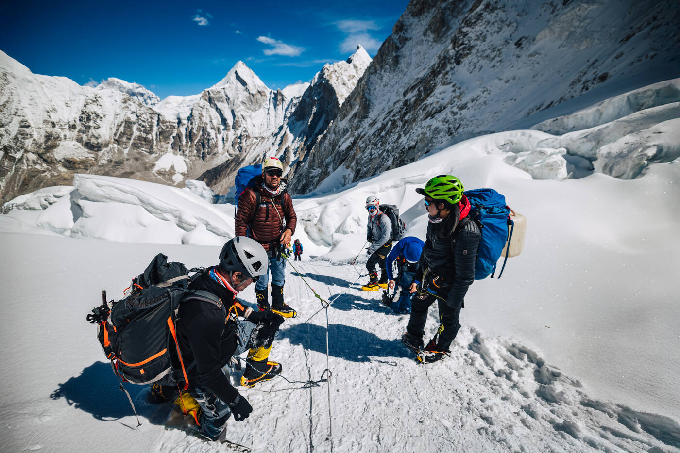 Climbers taking a rest break on snow with mountains behind in the upper Khumbu Icefall