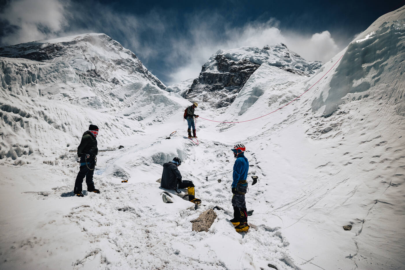 Four climbers at a rest point among ice formations in the Khumbu Icefall with mountains behind