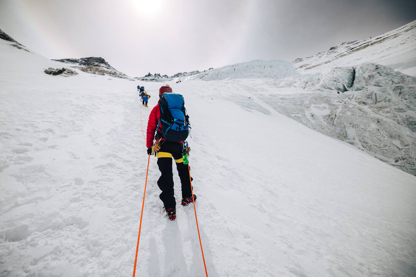 Roped climbers ascending a snow slope in hazy light