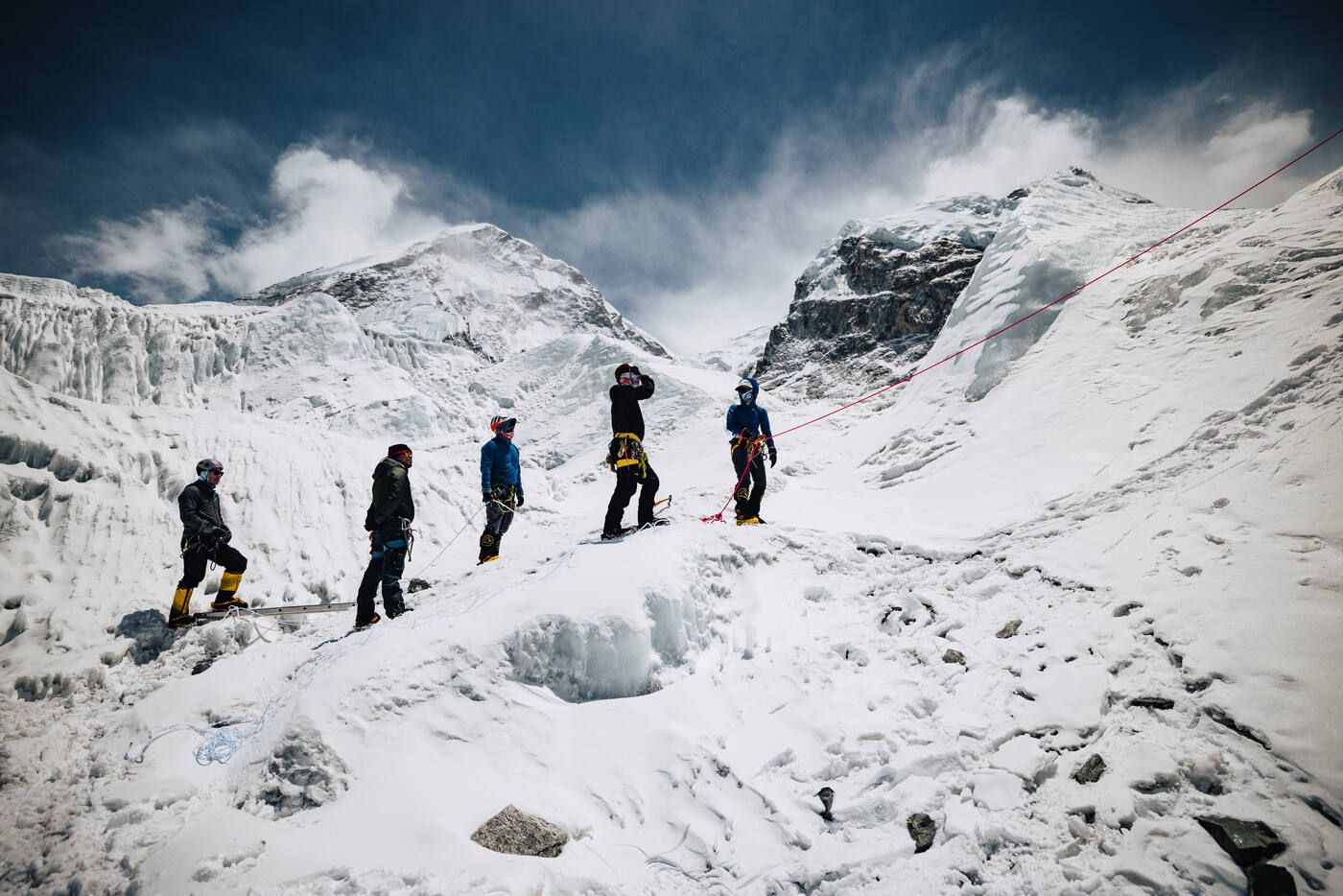 Five climbers walking in a line through the Khumbu Icefall among ice seracs