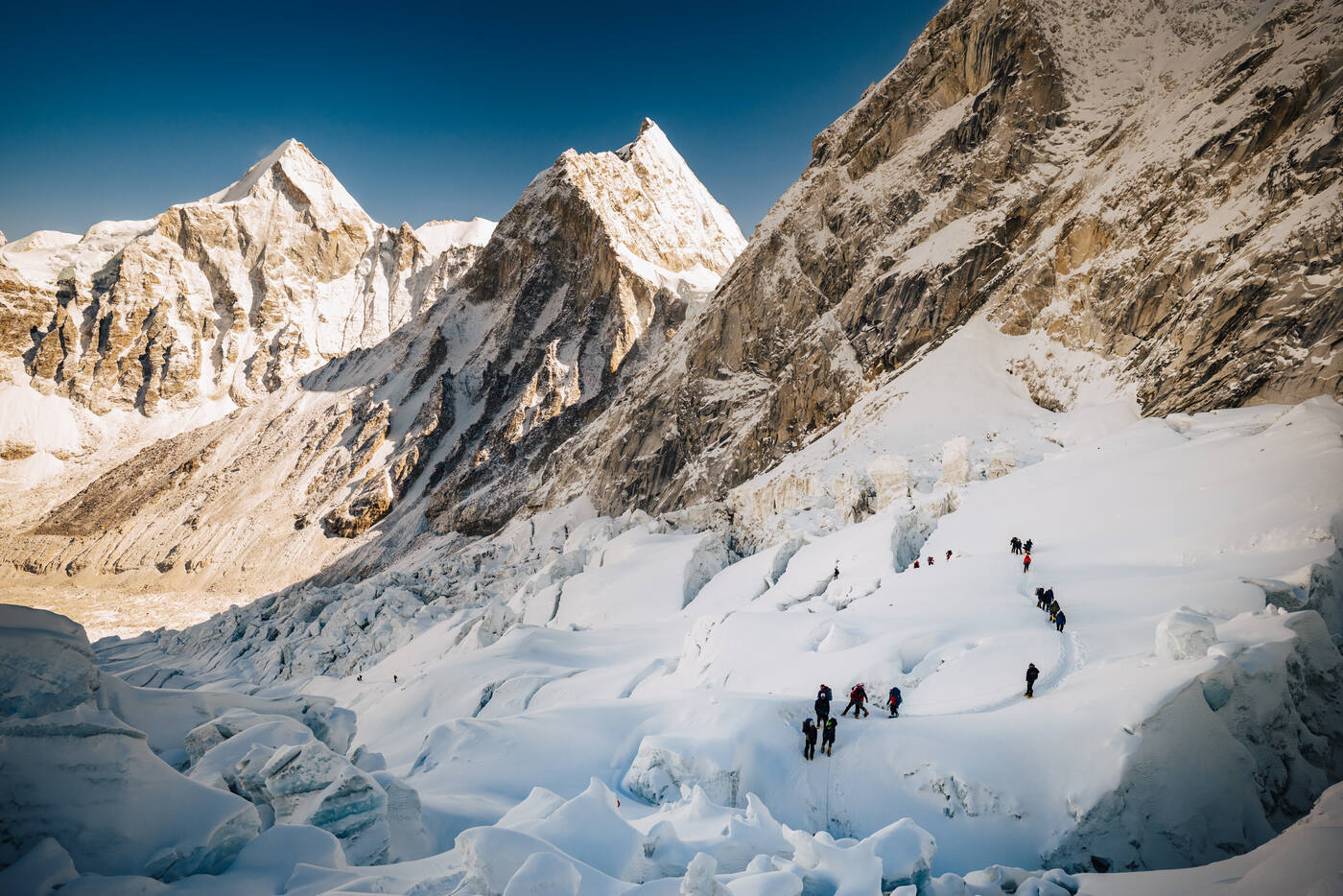 Climbers among ice seracs in the Khumbu Icefall with a dramatic peak behind
