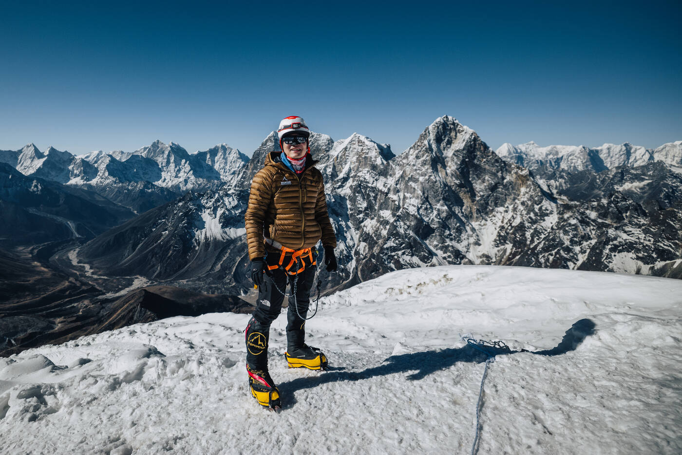 Jason standing on the snow-covered summit of Lobuche East at 6,119m with crampons and full mountaineering gear, Himalayan peaks in every direction