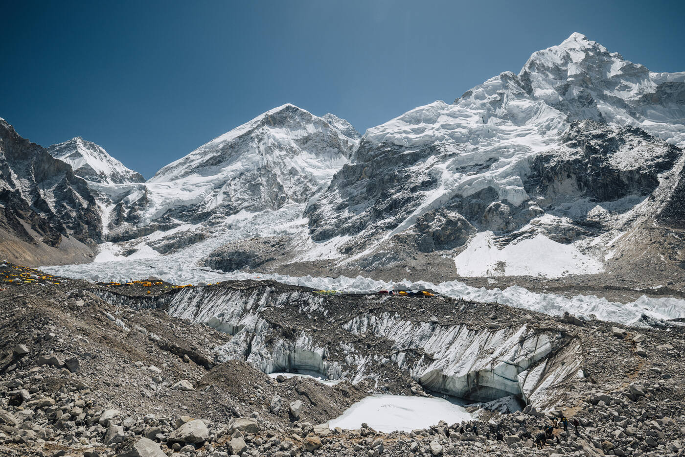 Panorama of the Khumbu Glacier from Everest Base Camp with snow-covered peaks and a frozen pond in the moraine