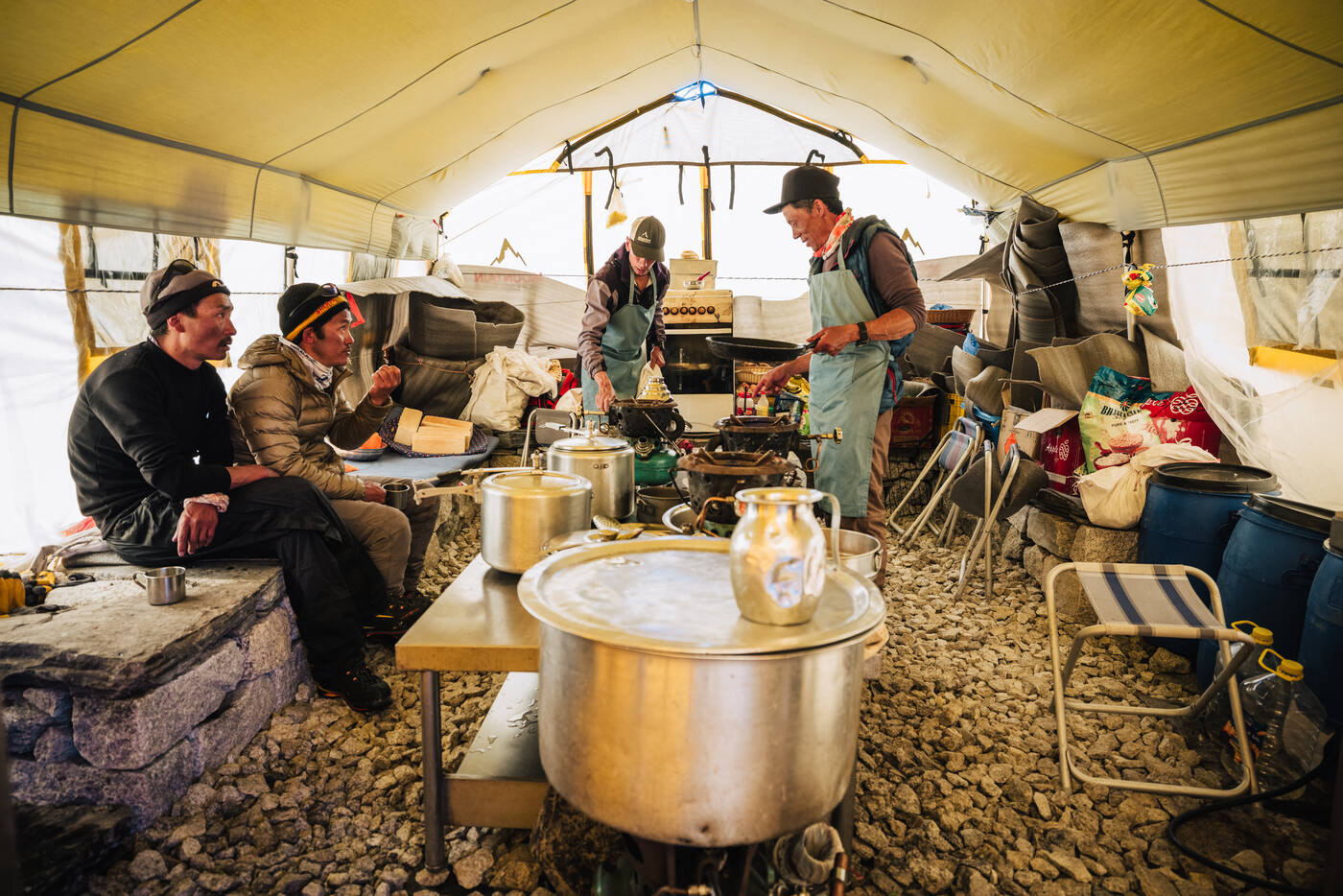 Inside the kitchen tent at Base Camp with cooks preparing food and steel pots on the table