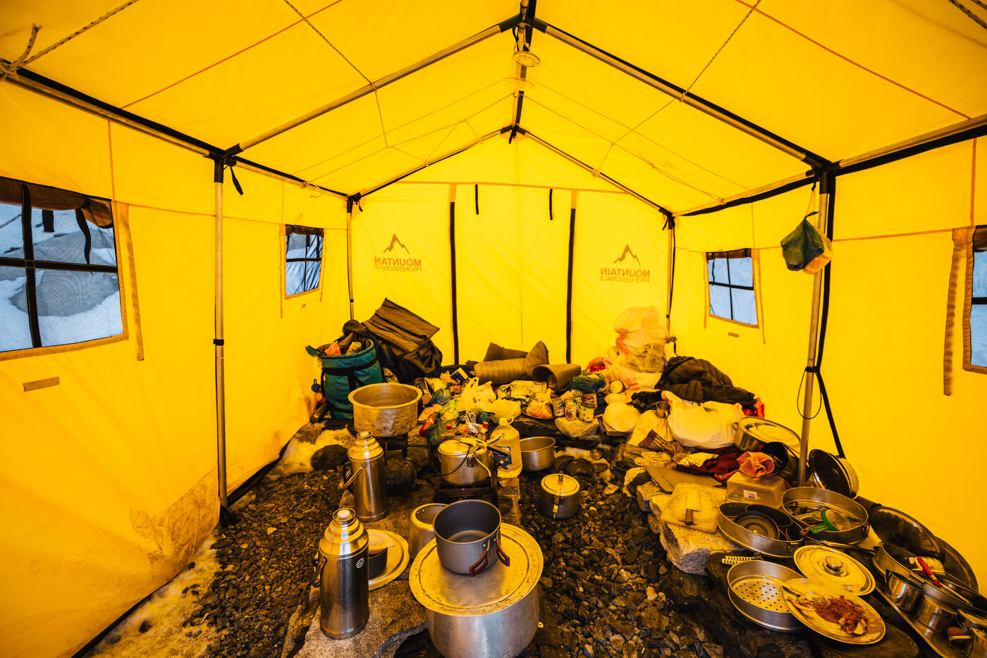 Interior of a yellow kitchen tent with steel pots and supplies on the ground