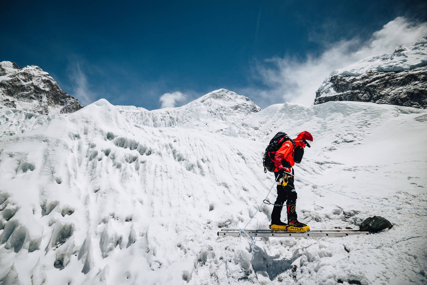 Climber crossing a ladder bridge over a crevasse in the Khumbu Icefall with ice walls on both sides