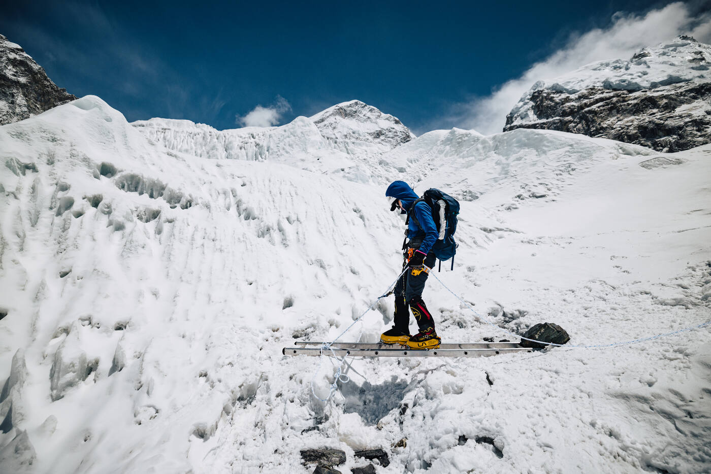 Climber crossing a ladder bridge over a crevasse in the Khumbu Icefall