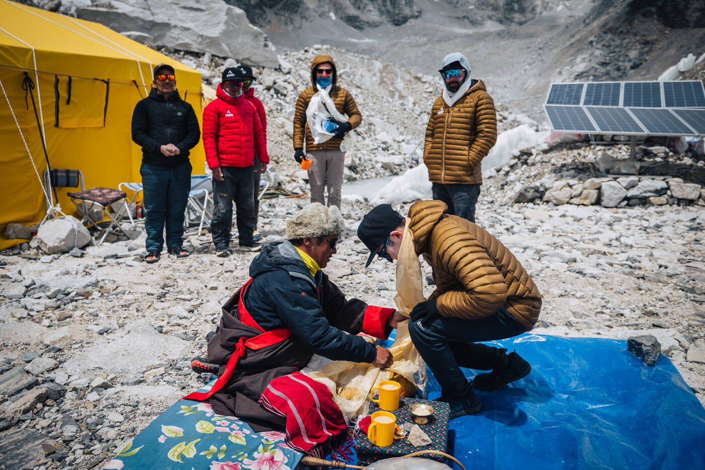 The lama handing a blessing to a kneeling climber during the Puja while team members look on