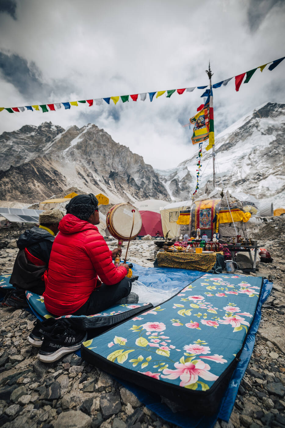 The lama seated with a drum at the Puja altar beneath prayer flags