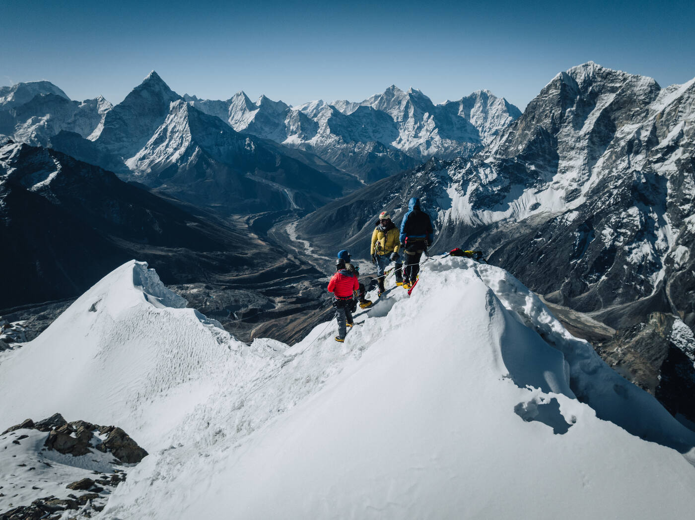Three climbers on the snow ridge of Lobuche East with a sea of Himalayan peaks behind