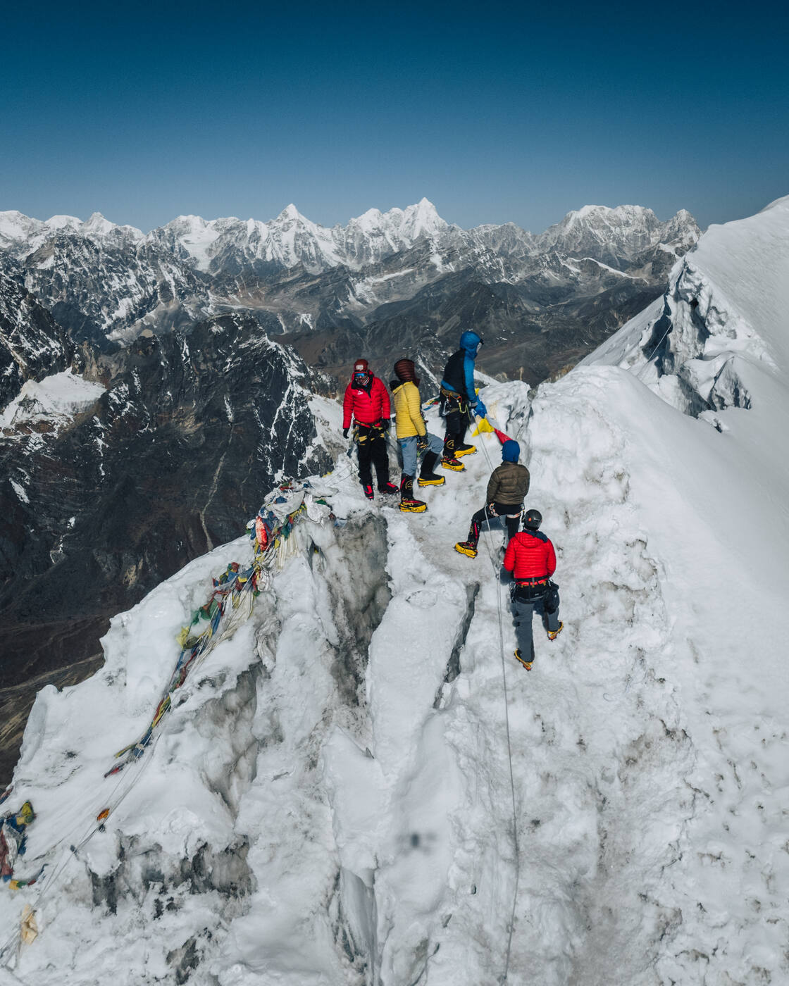Team members standing on the prayer-flag-lined snow ridge of Lobuche East