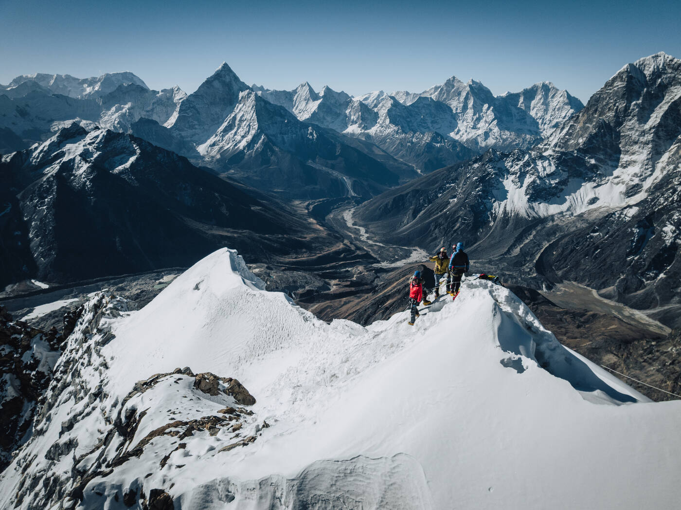 Climbers on the snow ridge of Lobuche East seen from above, with Himalayan peaks in the distance