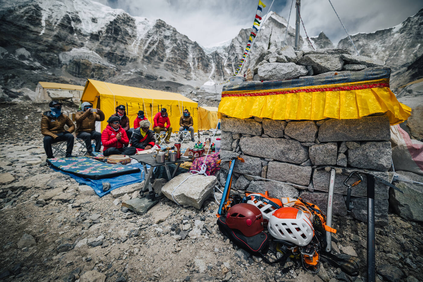 Climbing gear laid out before the stone Puja altar at Base Camp with the team seated nearby