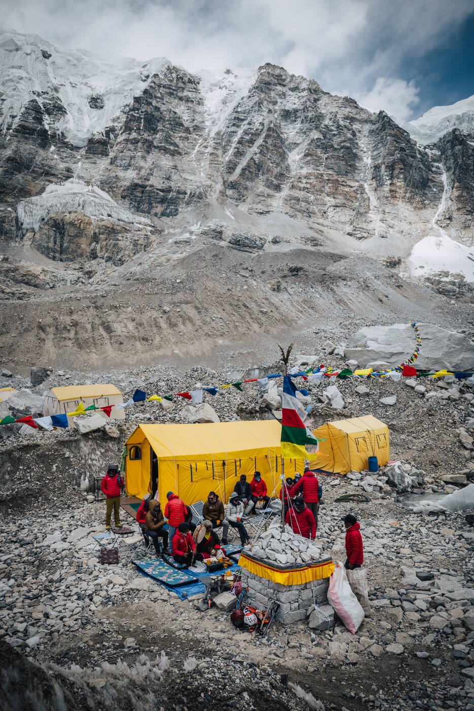 The Puja ceremony seen from above, with the team gathered around the altar and prayer flags beside the yellow tents