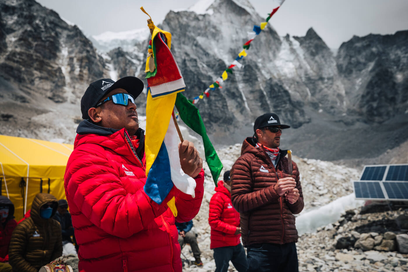 A Sherpa team member in a red jacket raising a prayer flag pole during the Puja ceremony at Base Camp