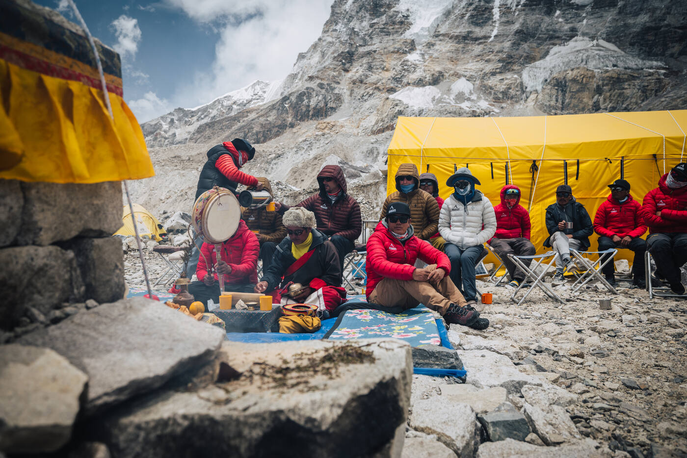 Team members seated around the drummer at the Puja ceremony beside the yellow tents