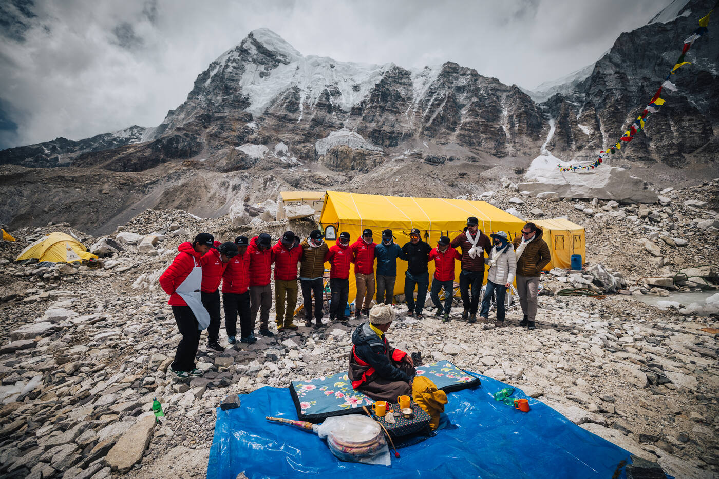 The team standing in a line before the seated lama at the Puja, yellow tent and peaks behind