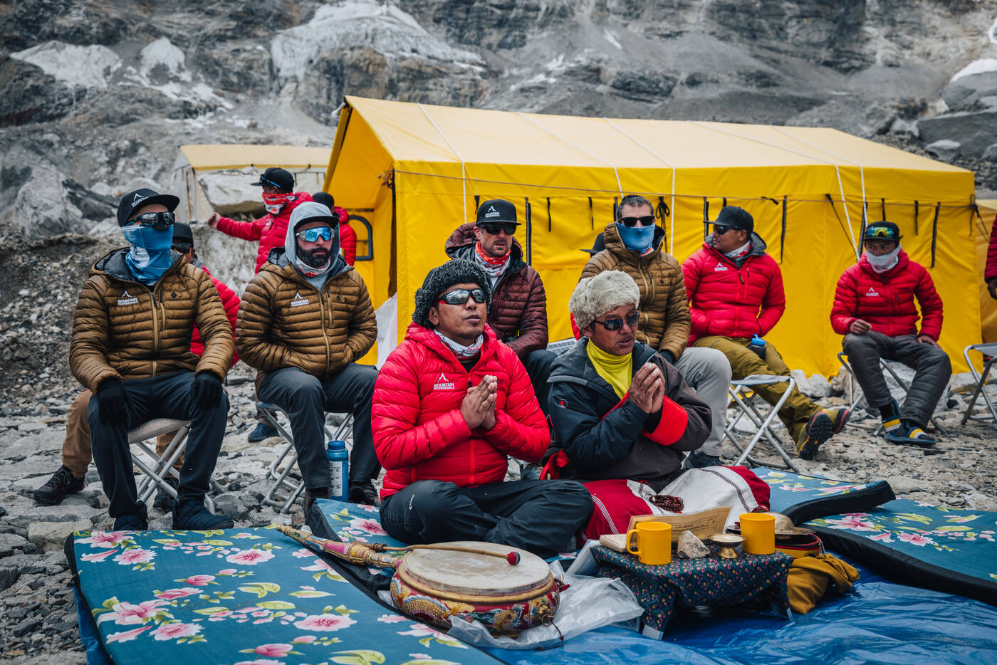 Team members seated in front of the yellow tent with hands pressed together in prayer during the Puja