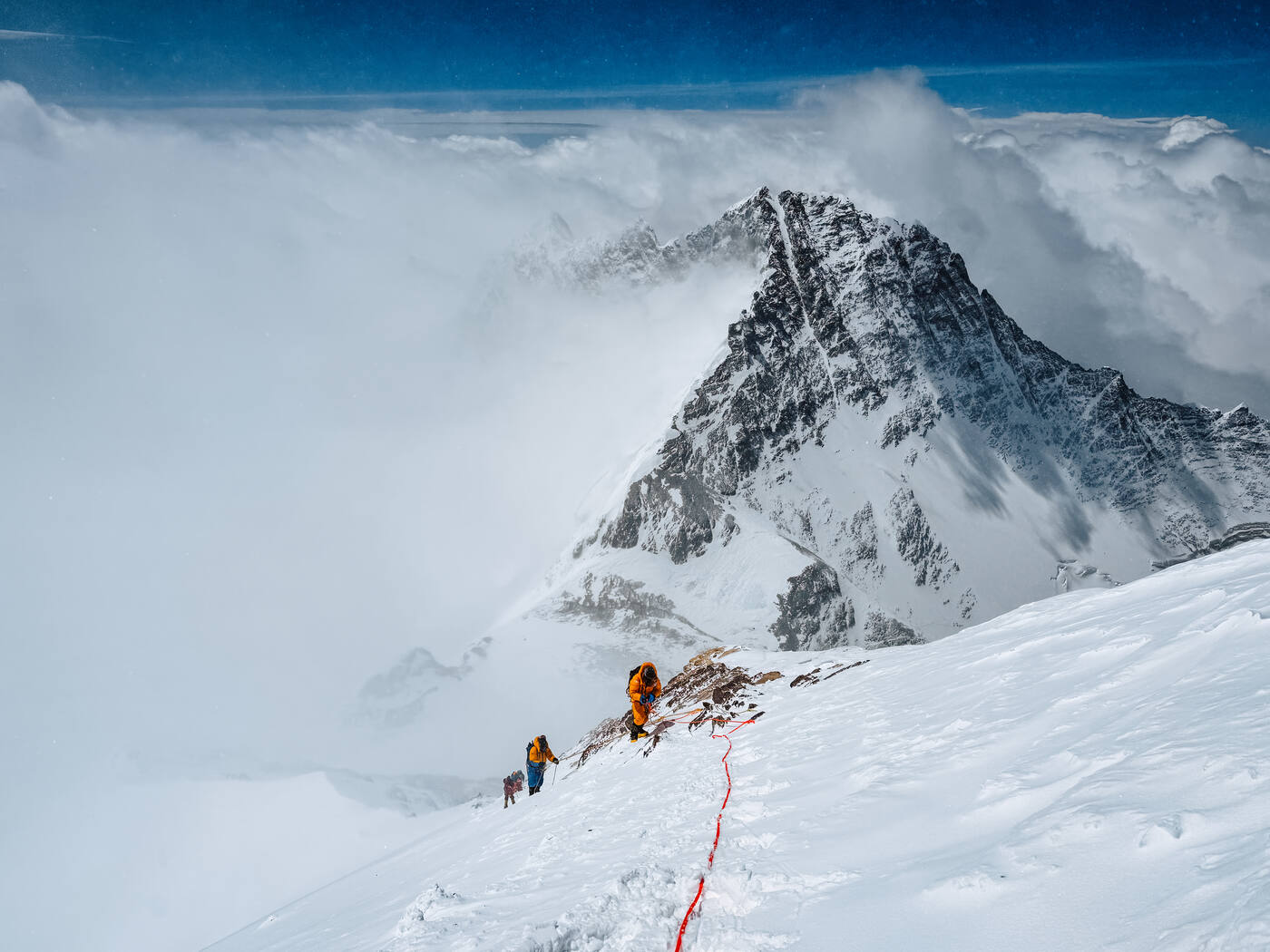 Climbing team ascending high on Everest with Lhotse and clouds visible far below