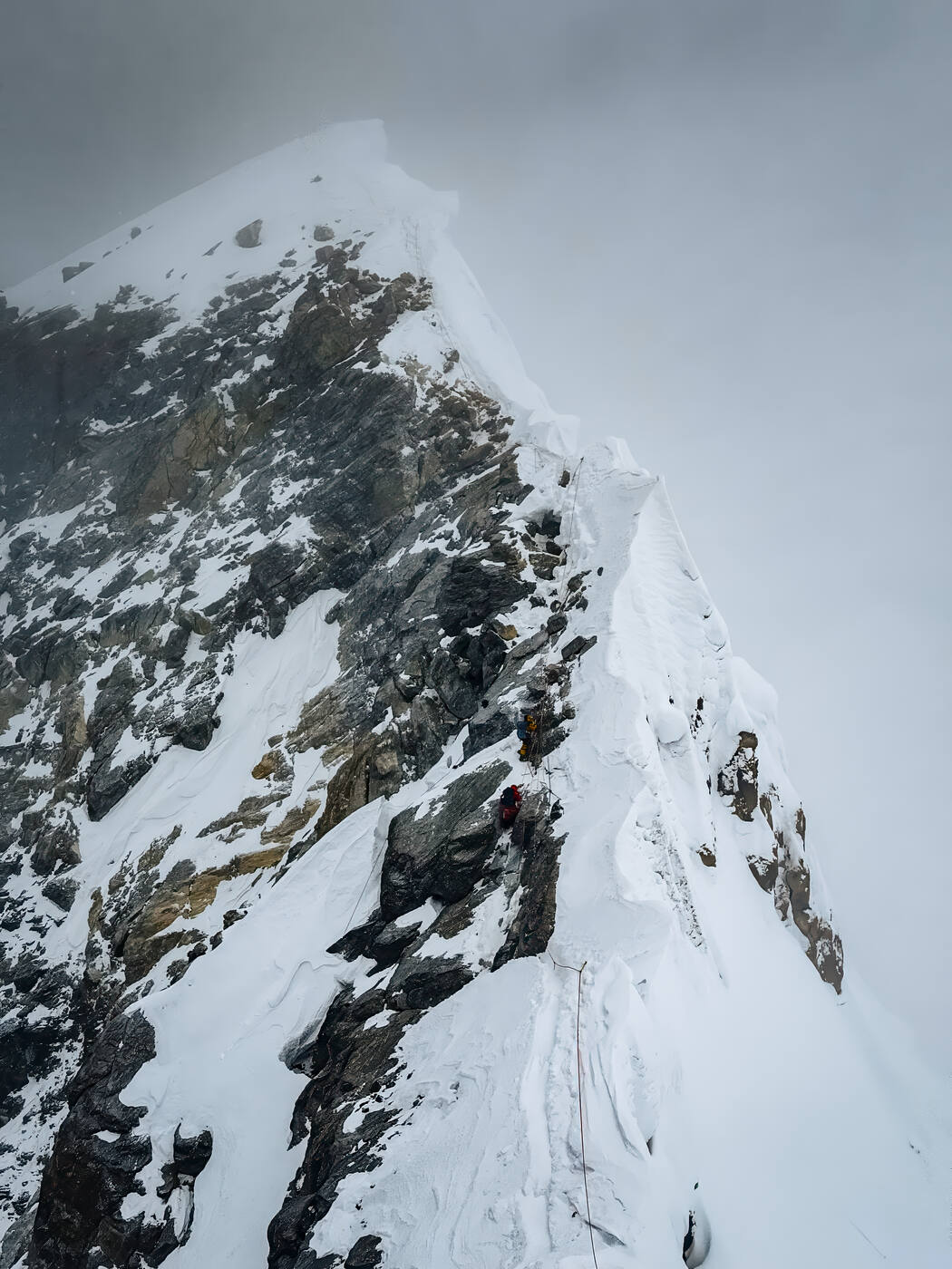 The Hillary Step area with rocky and icy terrain and climbers ascending through poor visibility