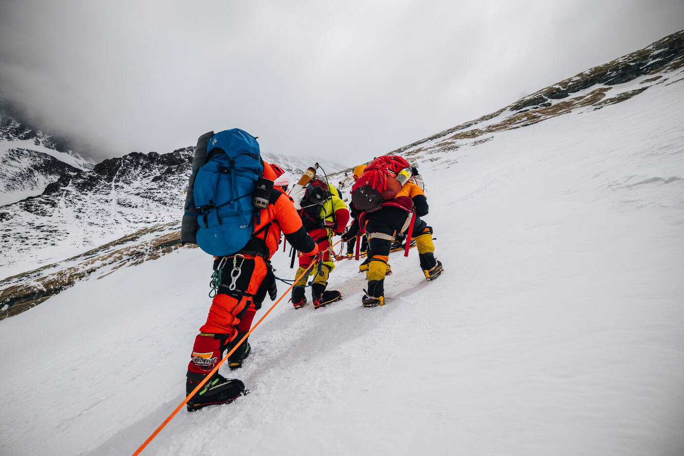 Climbers in down suits ascending a steep snowy slope on fixed ropes during the summit push