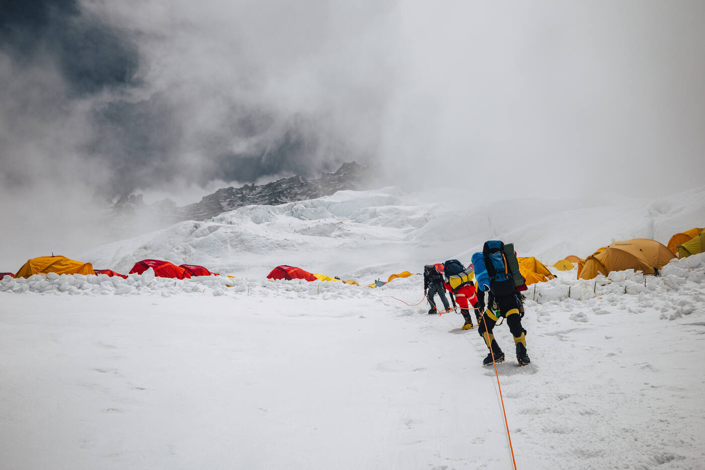 Climbers approaching a high camp with red and yellow tents in cloud and fog
