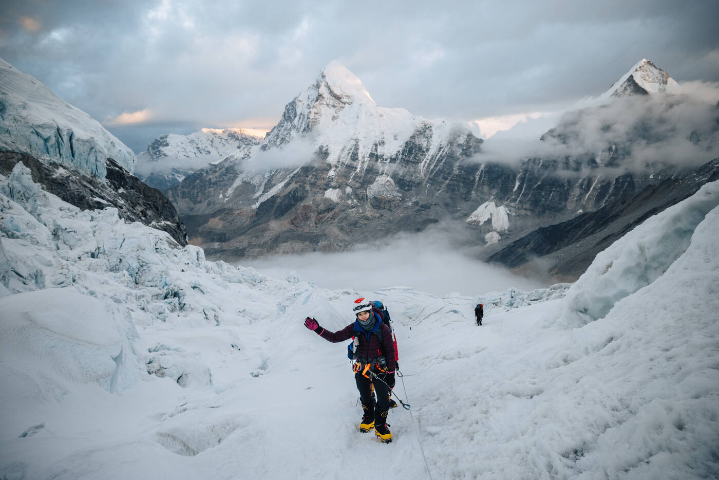 Climber in the Khumbu Icefall at dawn with a snow pyramid peak rising through clouds behind