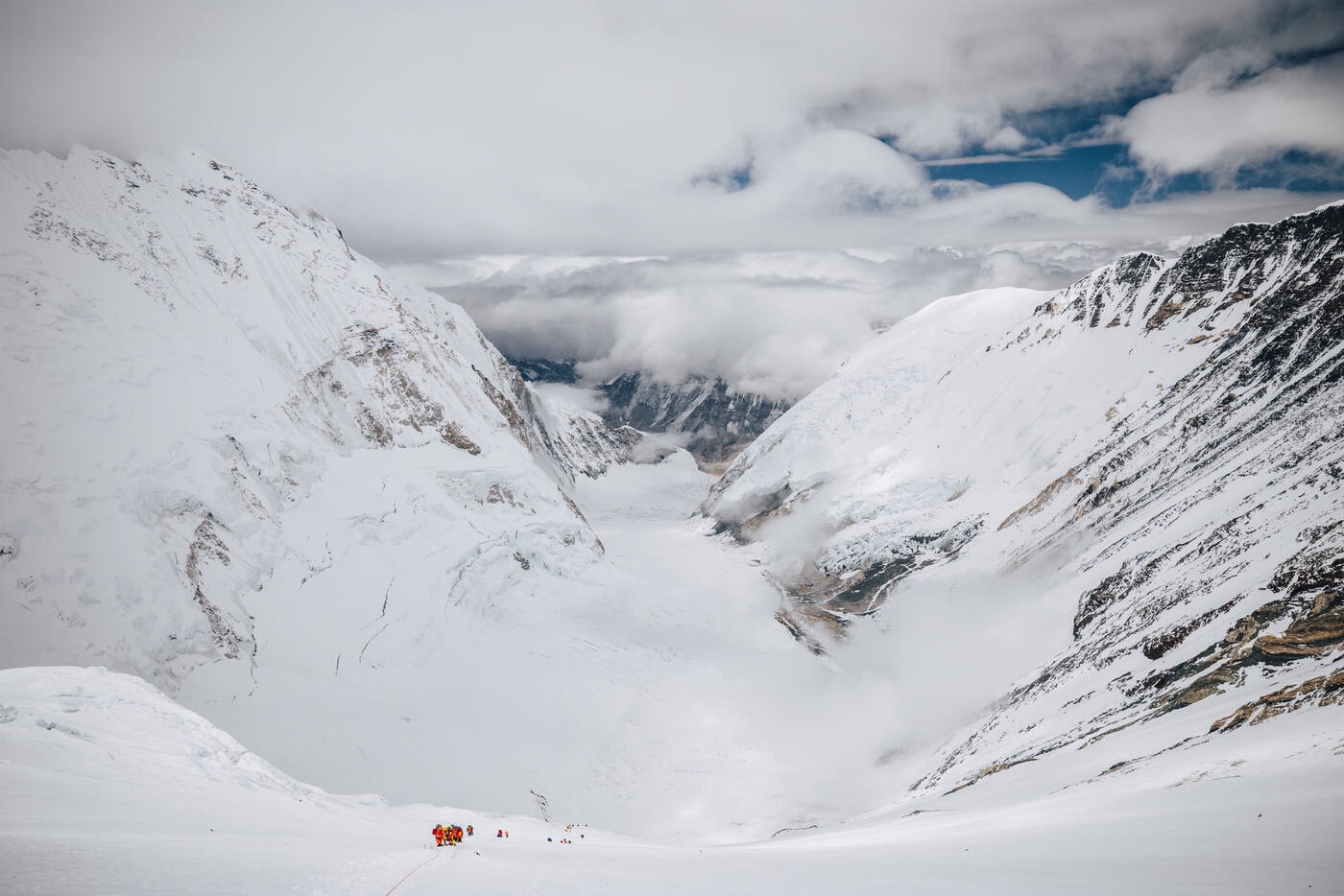 Looking down the Western Cwm from high on the Lhotse Face with a few climbers on the snow below and cloud filling the valley