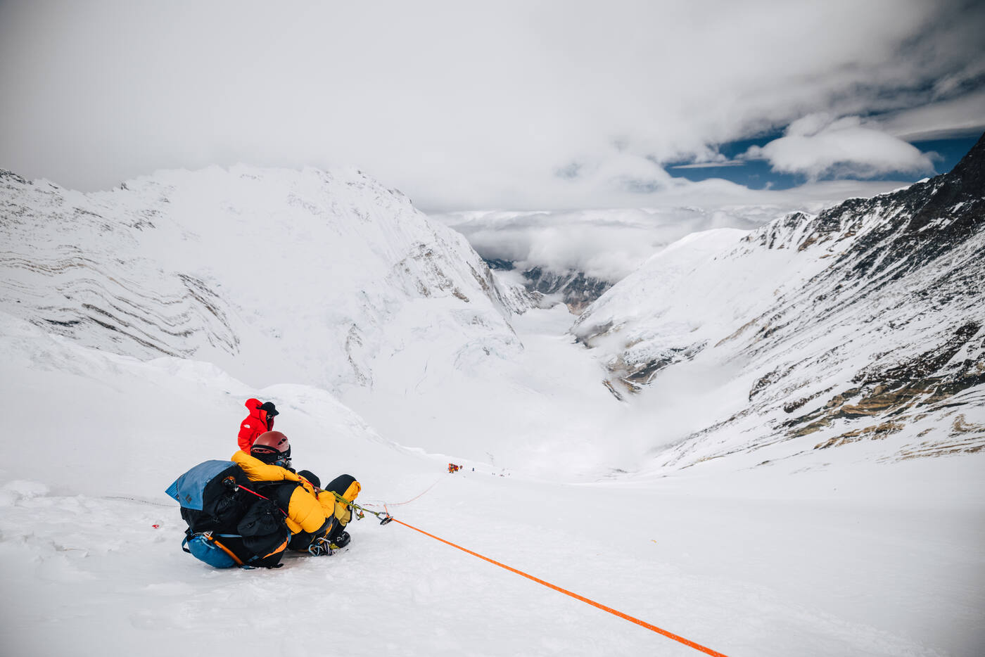 Climbers resting on a snow slope looking down the cloud-filled Western Cwm