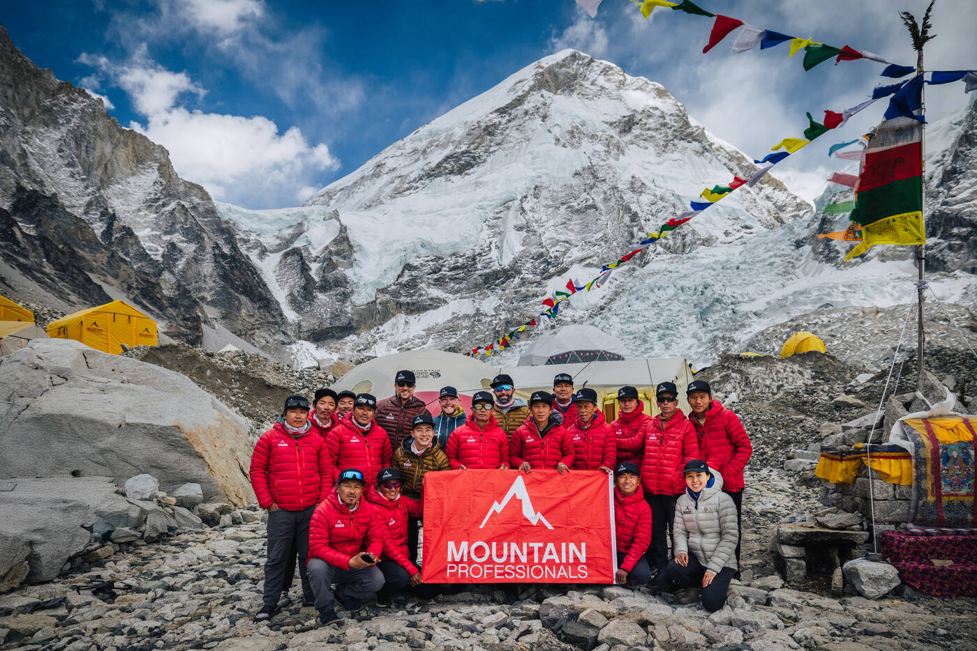 Full Mountain Professionals team posing with red banner at Everest Base Camp with Khumbu Icefall behind