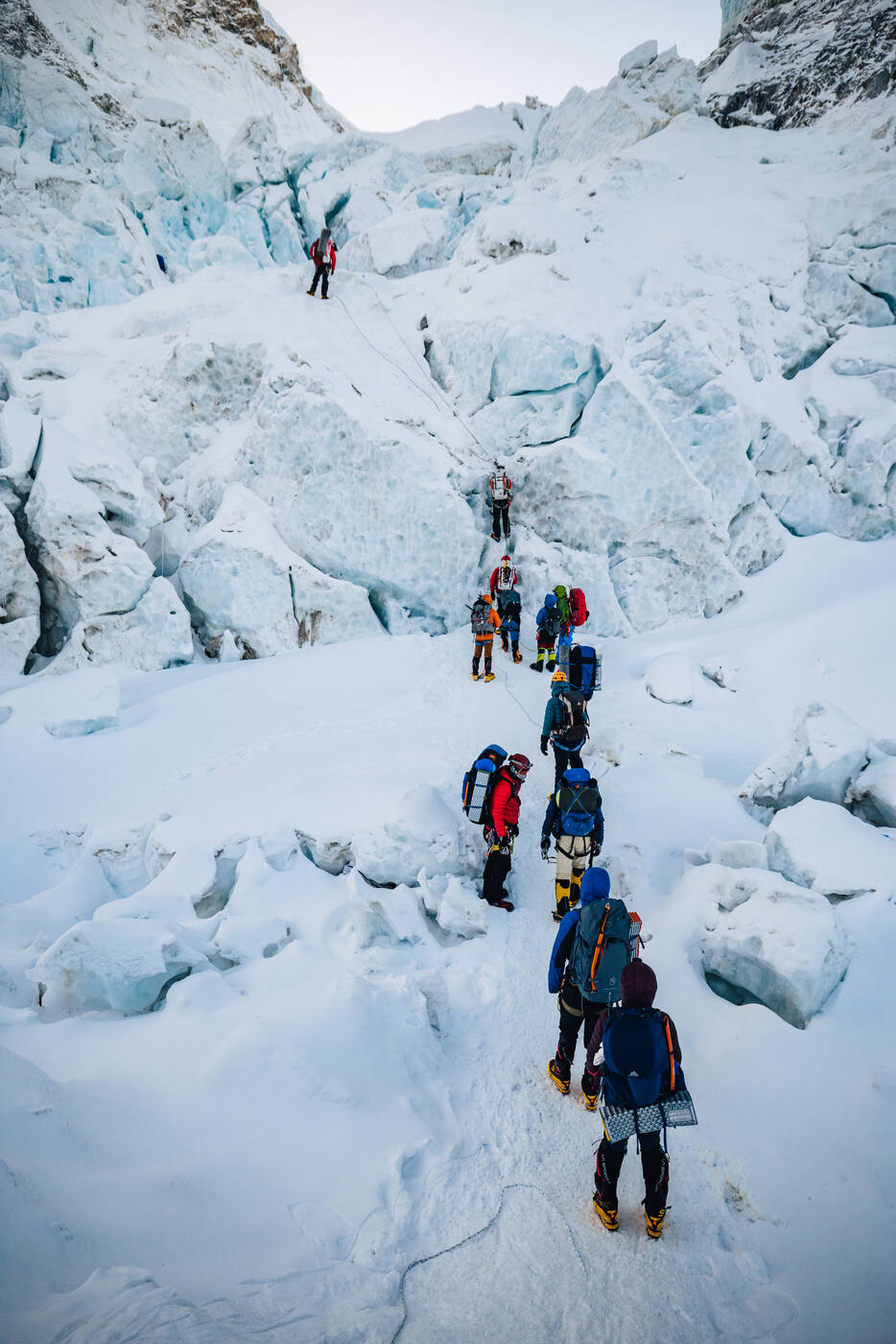A line of climbers ascending through the Khumbu Icefall between ice blocks