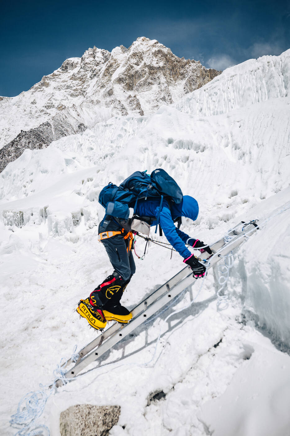 Climber stepping up a ladder against an ice wall in the Khumbu Icefall