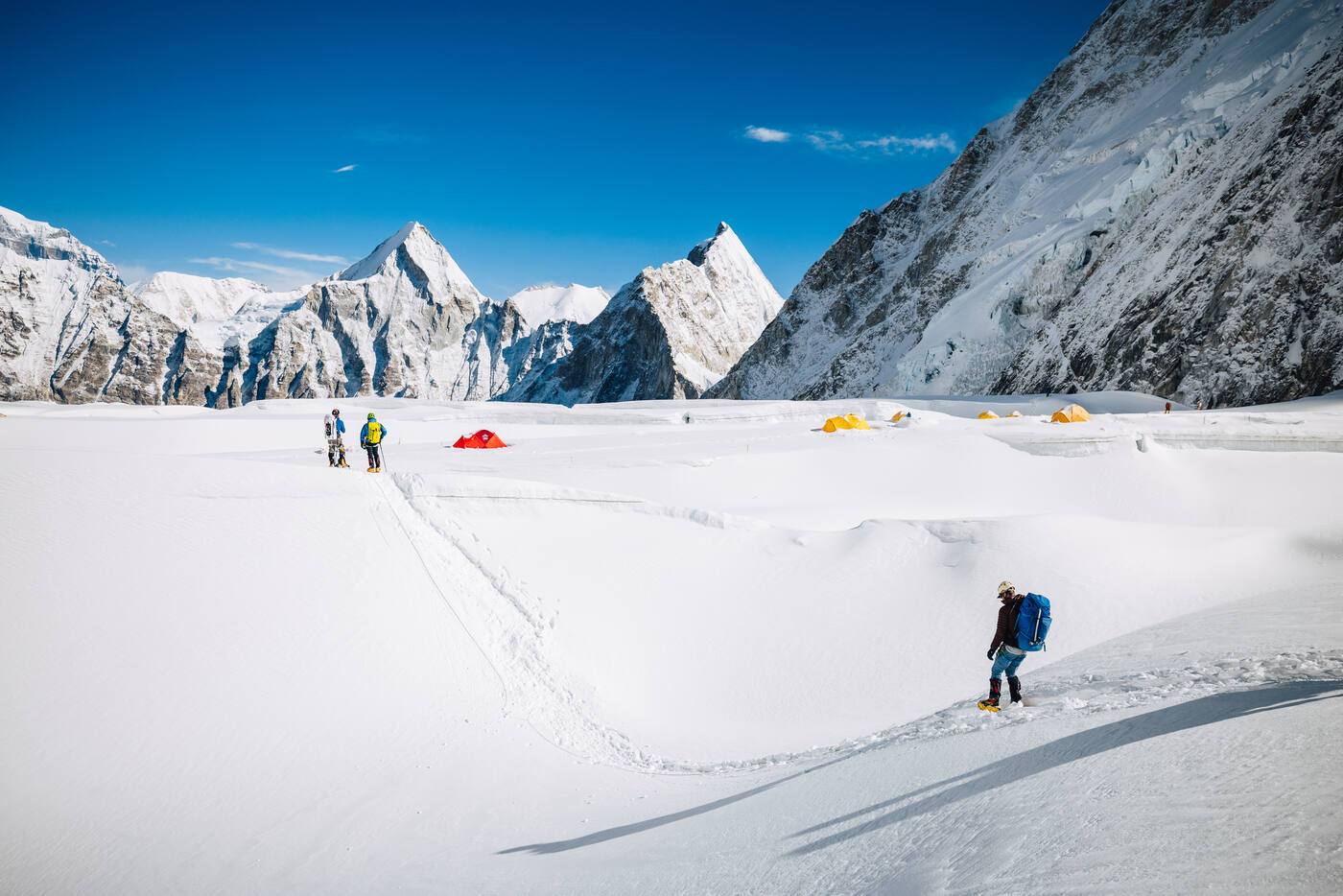 Climber walking on flat snow near Camp 1 in the Western Cwm with dramatic peaks and tents behind