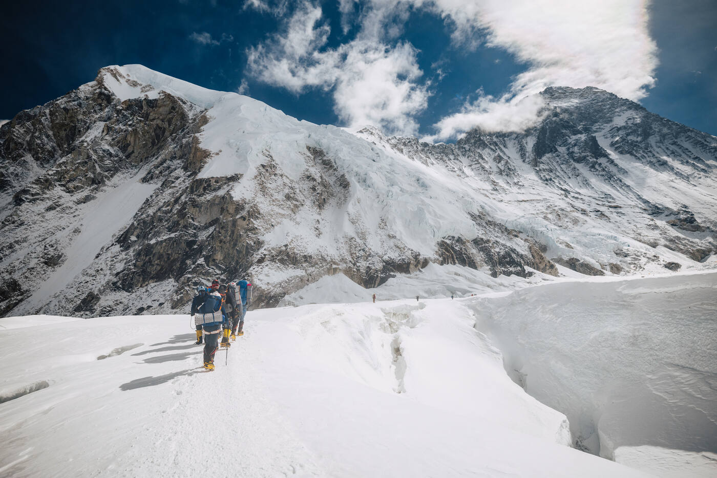 Climbers walking up a snow slope in the Western Cwm beside a large crevasse, with rocky peaks above