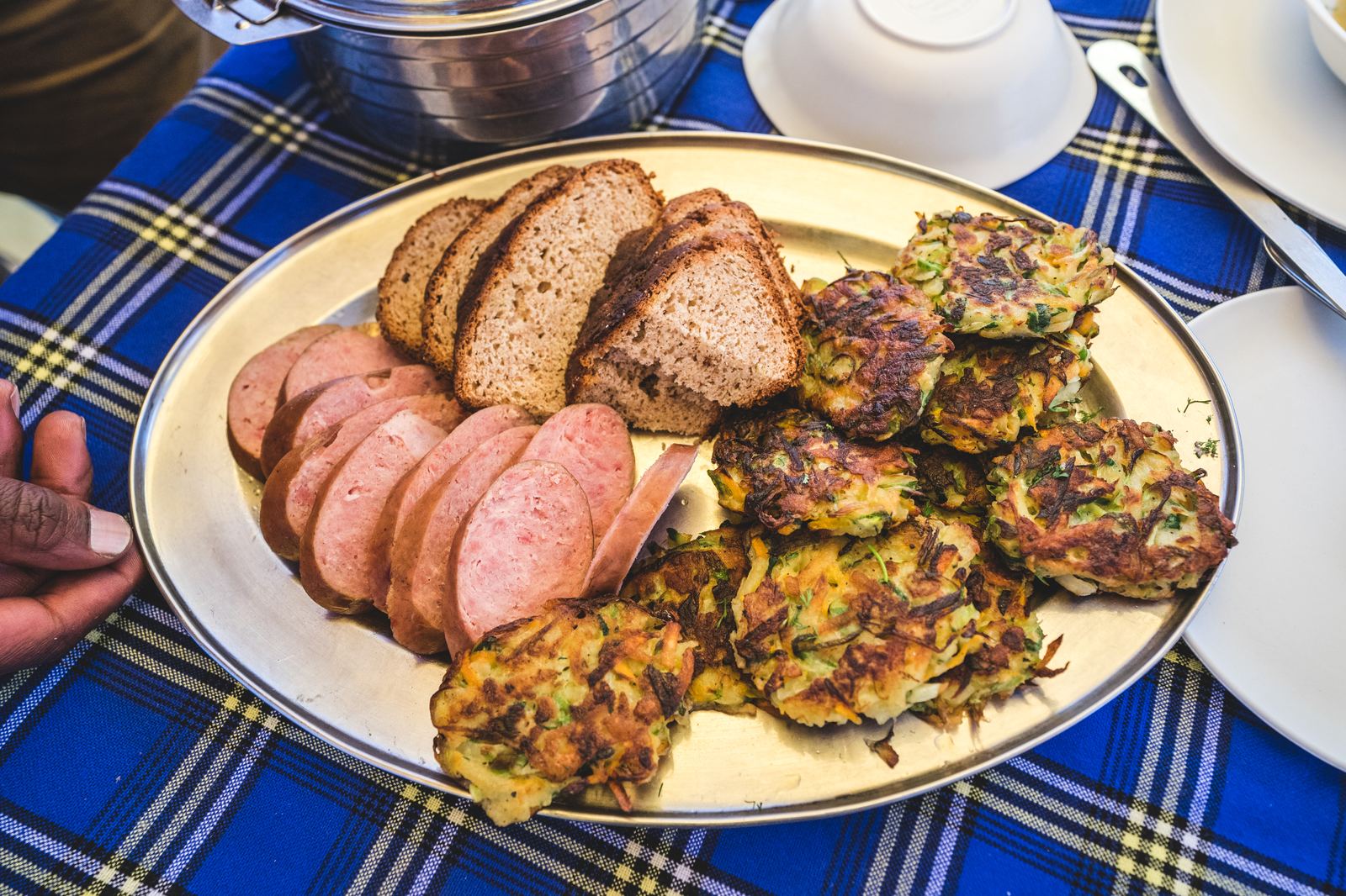 Camp meal spread with bread, sliced sausage, and fritters on a blue plaid tablecloth