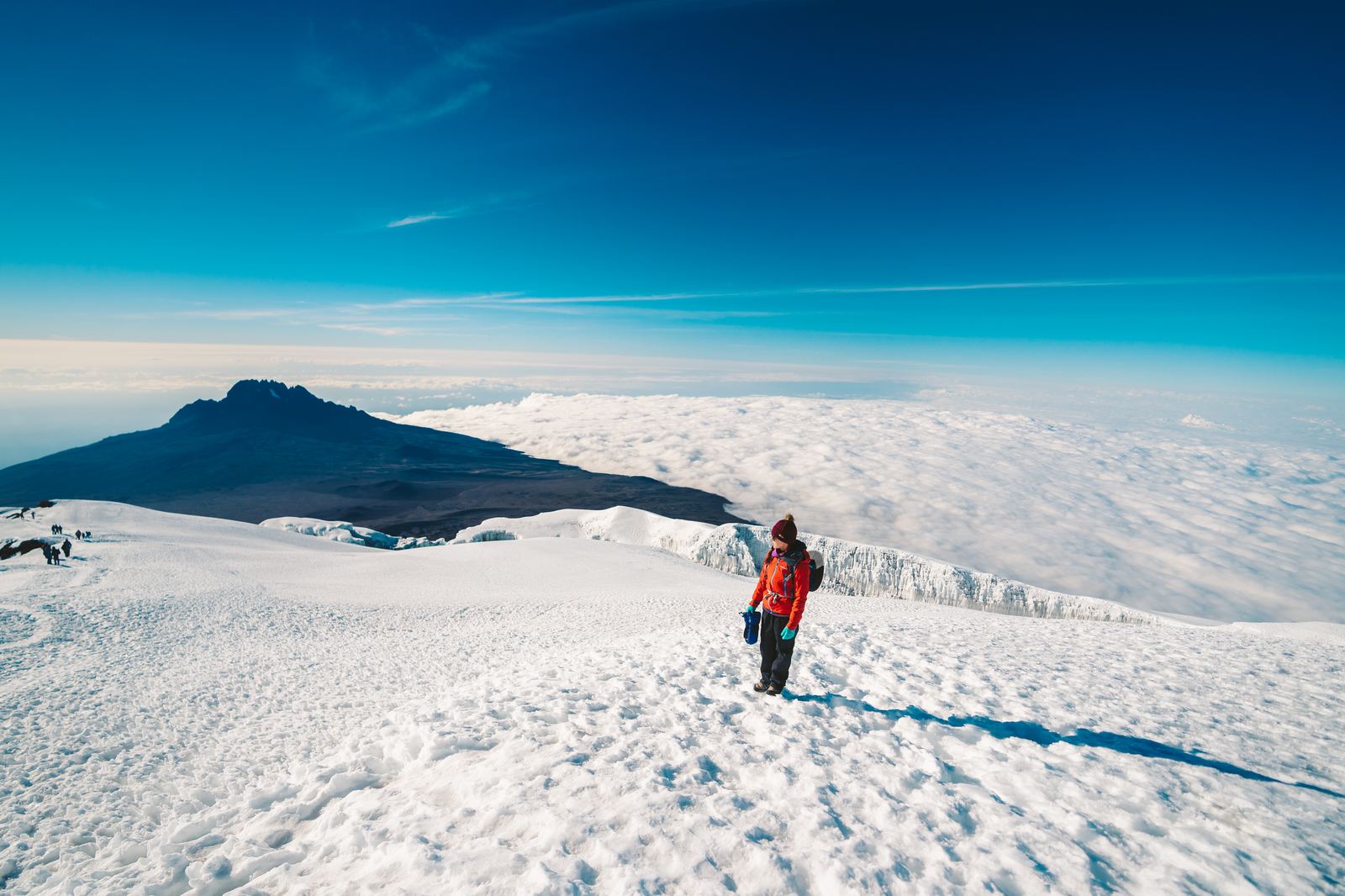 Hiker descending the snowy slopes of Kilimanjaro with Mawenzi Peak visible in the distance