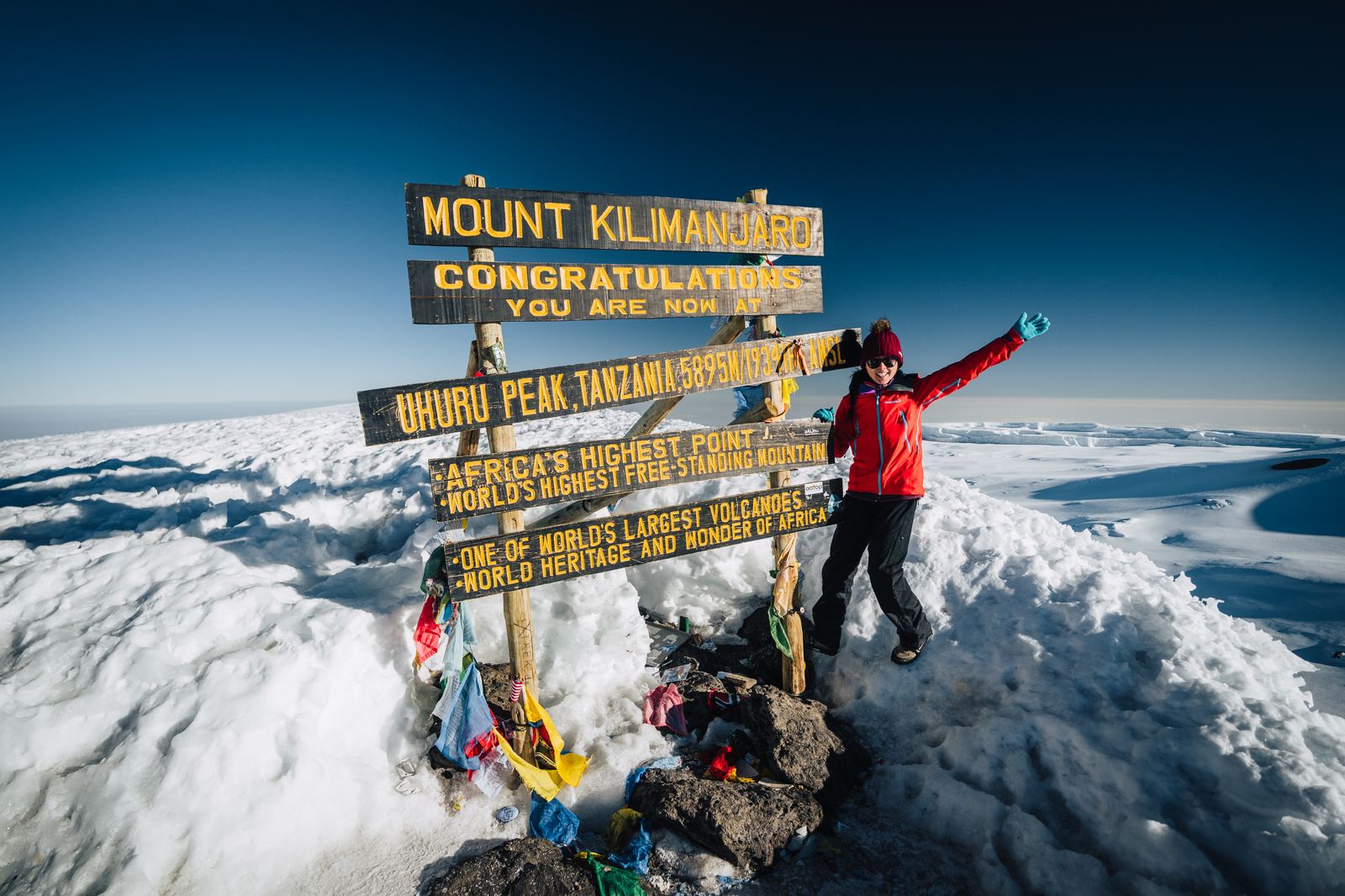 Grace celebrating at the Uhuru Peak summit sign on Mount Kilimanjaro