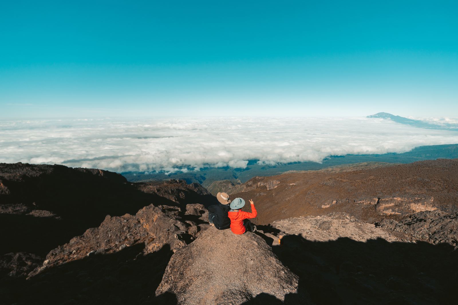 Climbers resting on a rocky outcrop above an ocean of clouds on Kilimanjaro