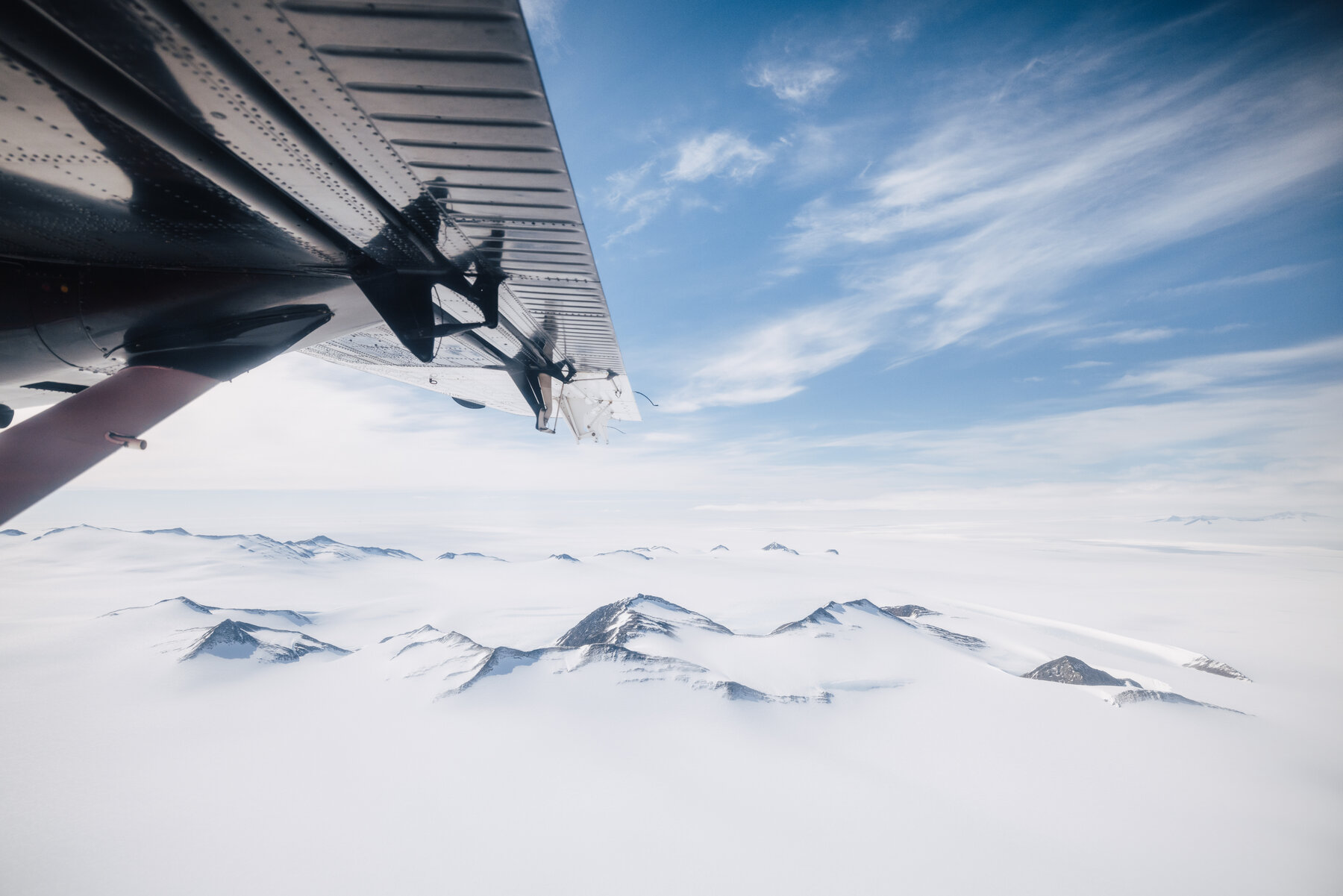 Aerial view from airplane wing over Antarctic ice sheet and snow-covered peaks
