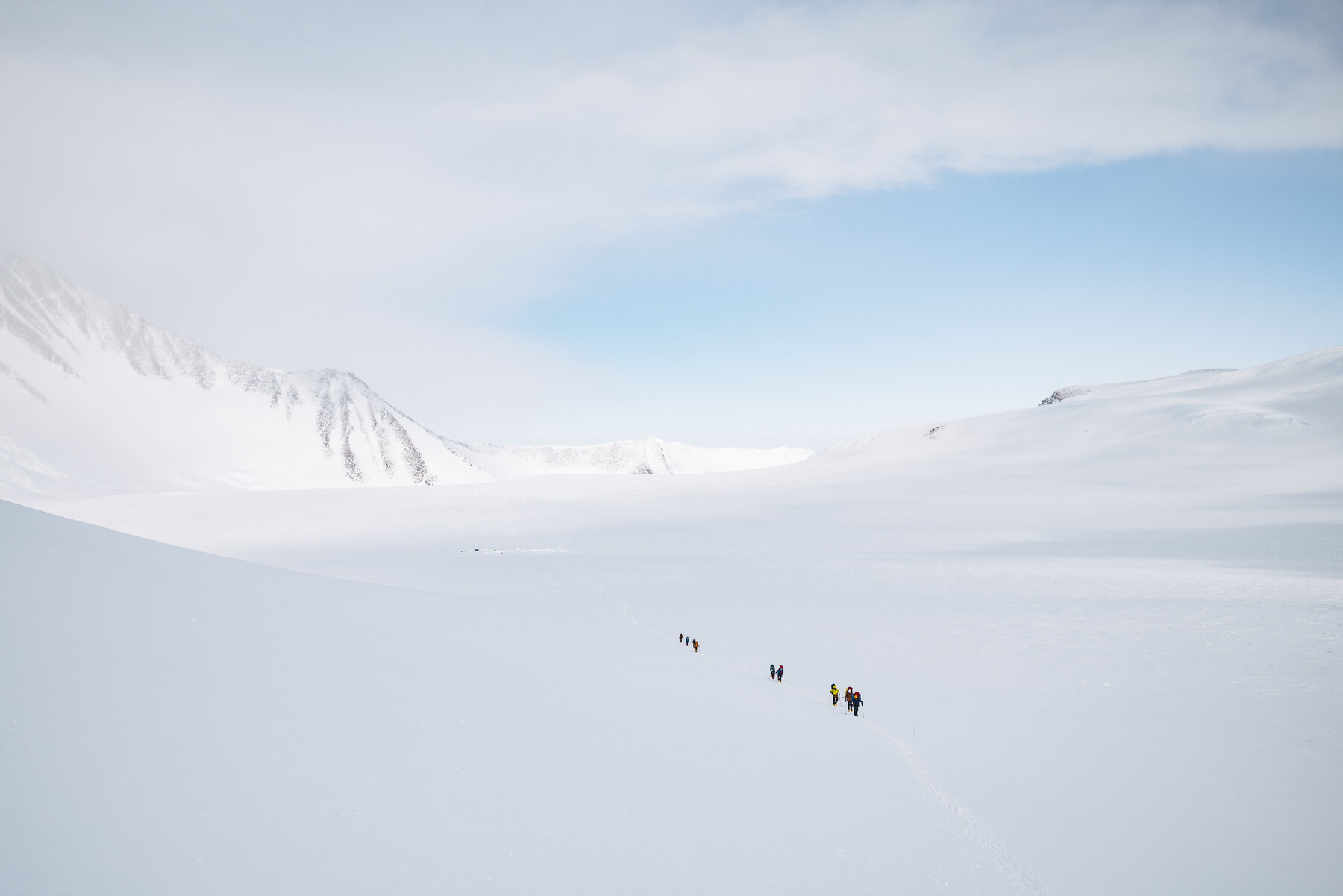 Line of climbers crossing a vast snow field on Vinson with mountain walls on either side