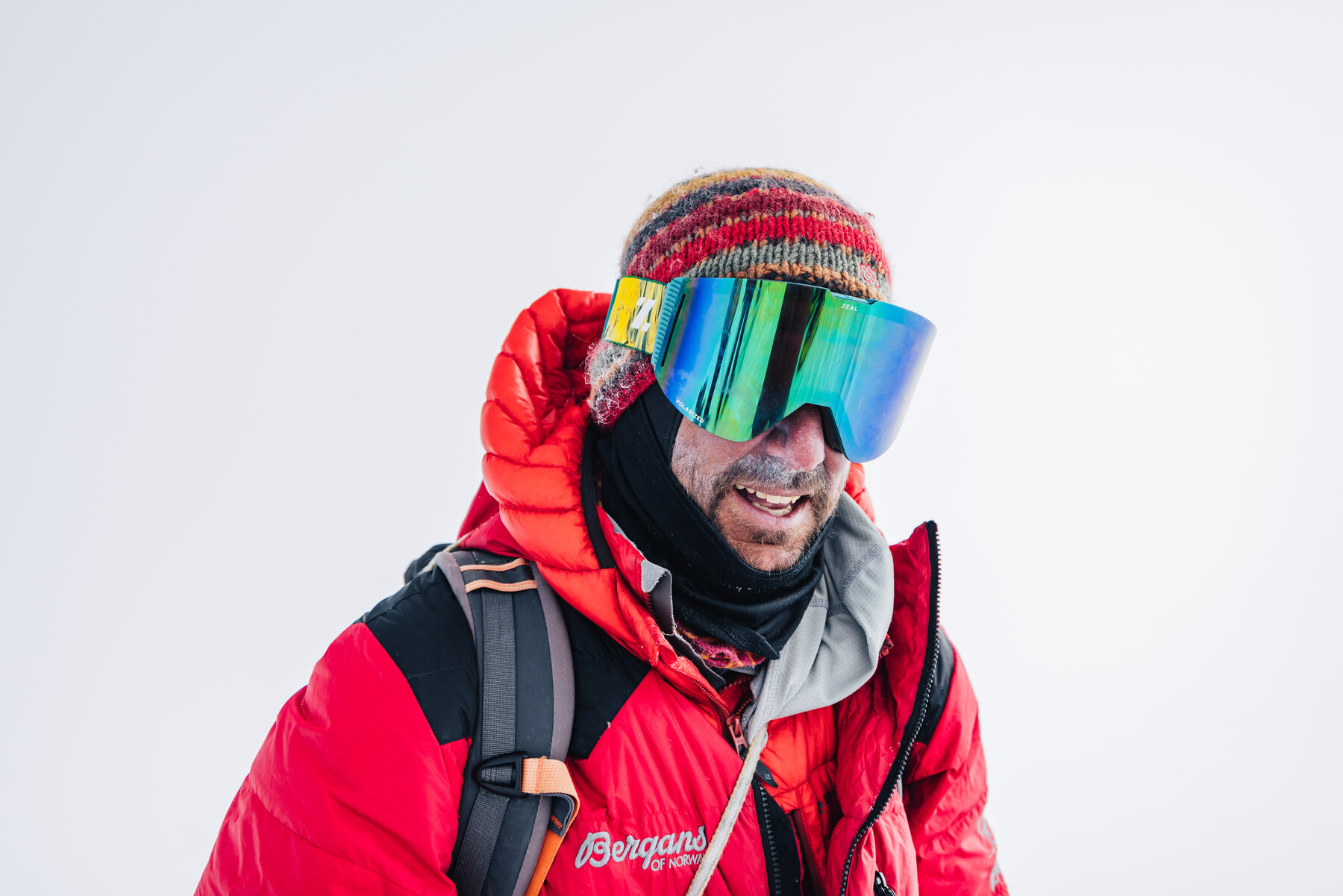 Smiling climber in a red down jacket, knit beanie and mirrored goggles at Union Glacier
